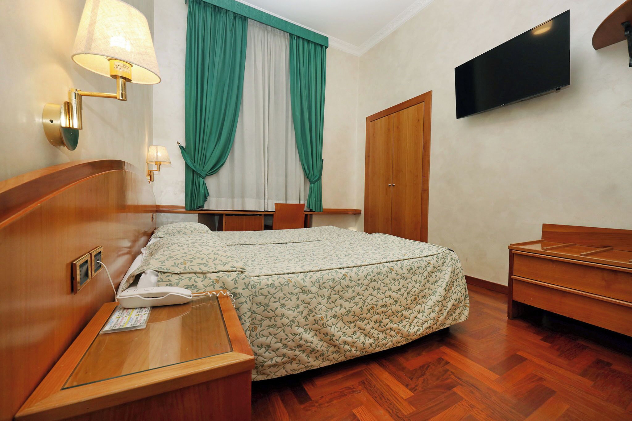A hotel room with a bed, bedside table, lamp, TV, and a wardrobe.