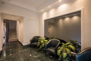 A hallway with a marble floor, two leather chairs, and potted plants. - Tito (Rome)