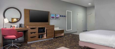 Habitación de hotel con cama, escritorio con computadora, televisor, microondas, cafetera y espejo.