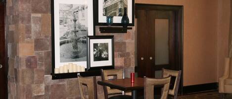 A dining area with a stone wall, framed pictures, a table with chairs, and a door in the background.