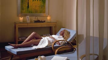A spa room with two massage tables, a painting on the wall, and a small table with candles and a teapot.
