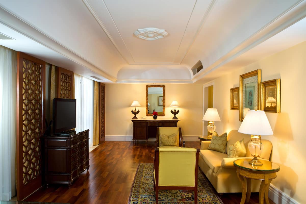 Habitación de hotel con piso de madera, un sofá, una silla, un escritorio con espejo y dos lámparas.