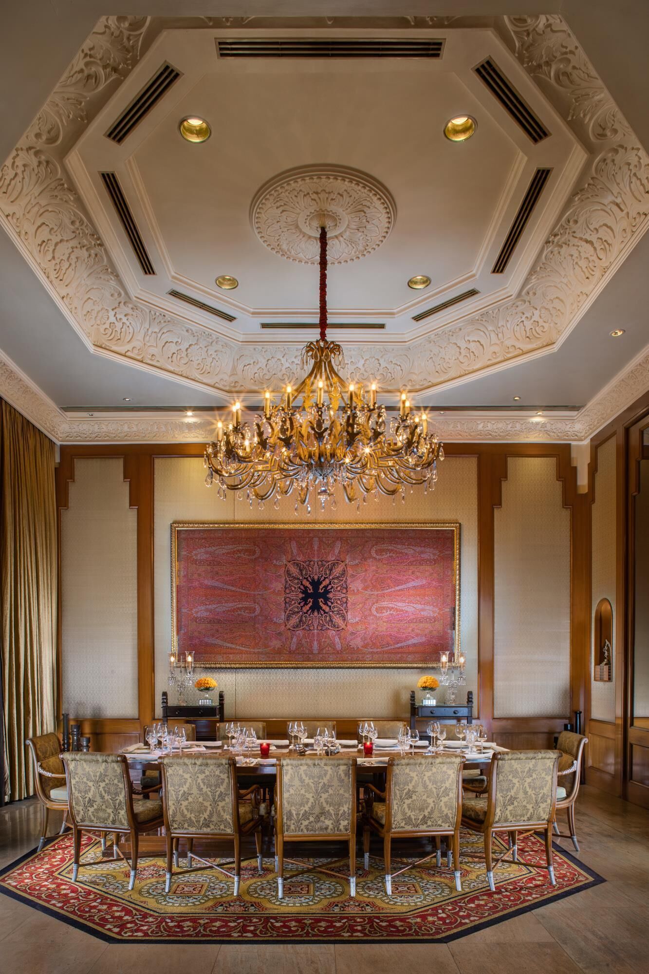 Une salle à manger élégante, dotée d’un grand lustre, d’un plafond orné et d’un grand élément décoratif mural.