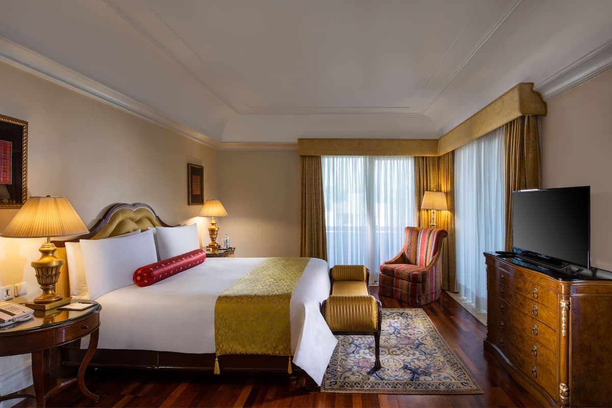 Una habitación de hotel con una cama grande, lámparas de noche, un televisor, un aparador y una silla.