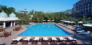 Relax by the pool surrounded by lush greenery and a classical building.