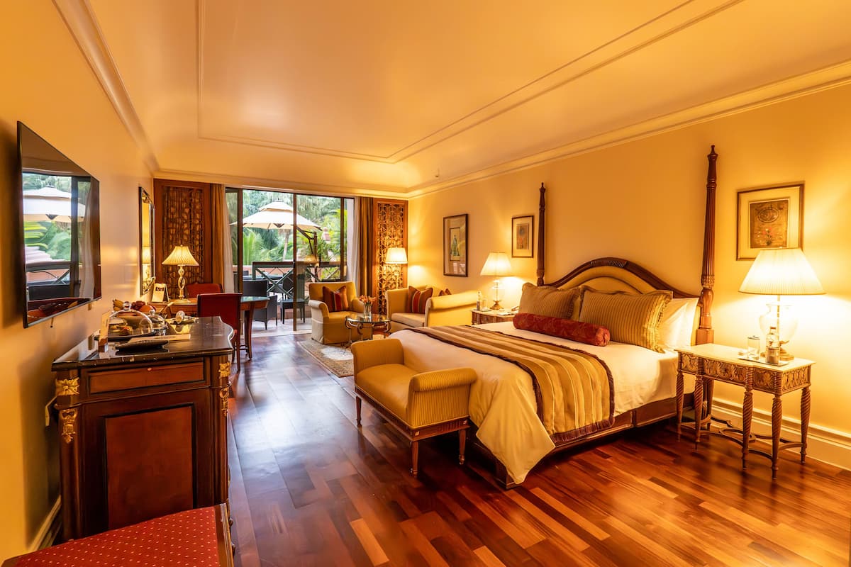 Un dormitorio espacioso con una cama grande, un área de estar con sofá y sillones, una mesa de comedor y vistas al exterior.
