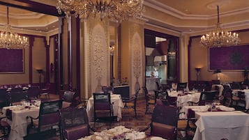 A formal dining room with multiple tables set for service, ornate chandeliers, and a classic interior design.