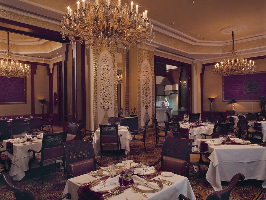 Un comedor formal con varias mesas dispuestas para el servicio, candelabros ornamentados y una decoración clásica.