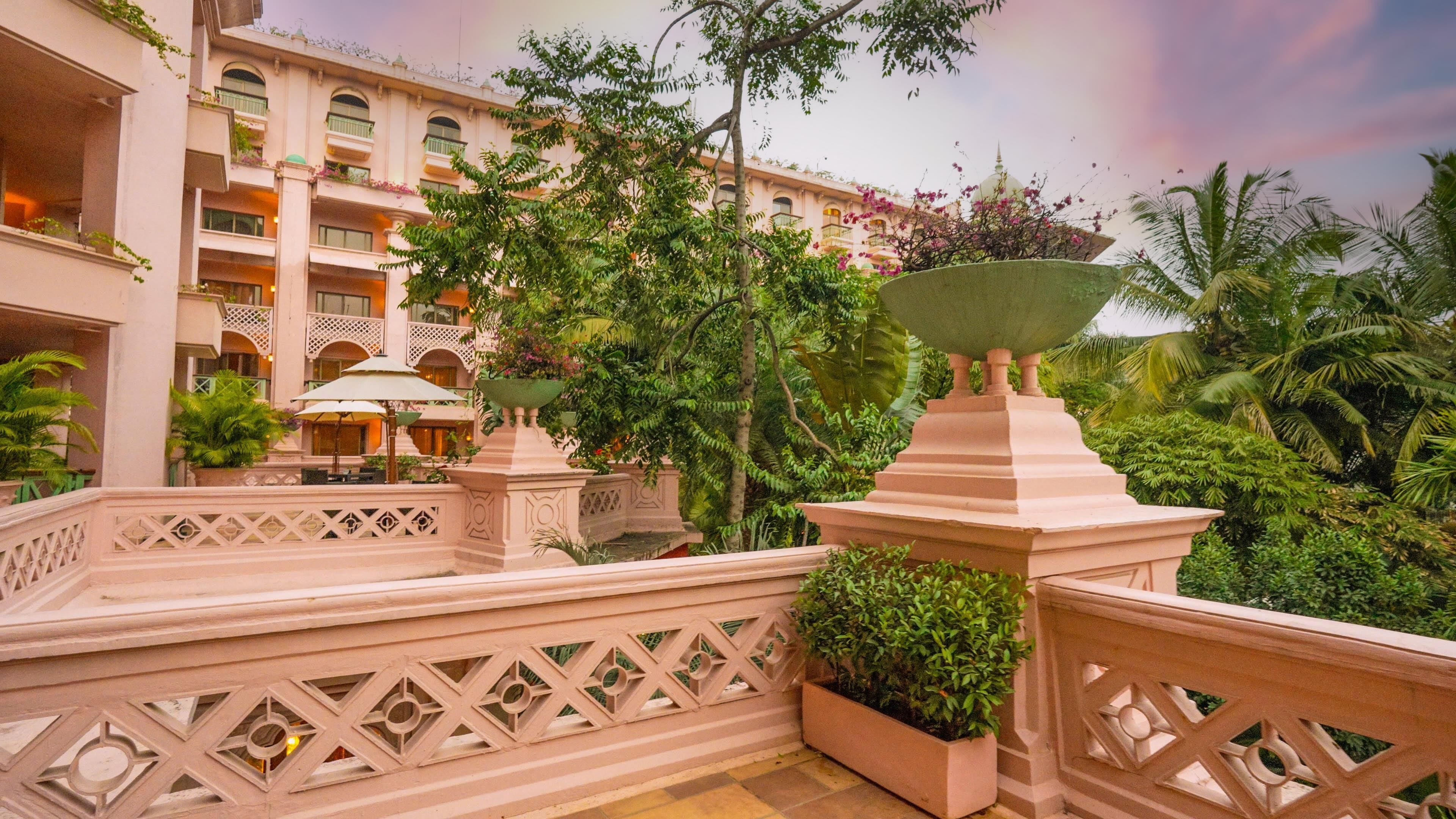 A hotel courtyard with a central water feature, surrounded by lush greenery and a multi-story building with balconies.