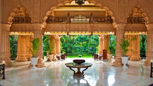 A grand lobby with ornate columns, a central table, and a view of a lush garden.