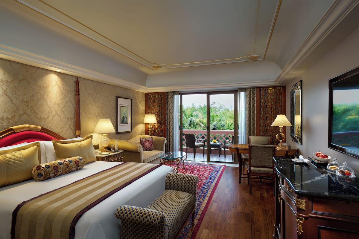 Habitación de hotel con una cama grande, un escritorio, una silla, una mesita y un balcón con vistas a zonas verdes.