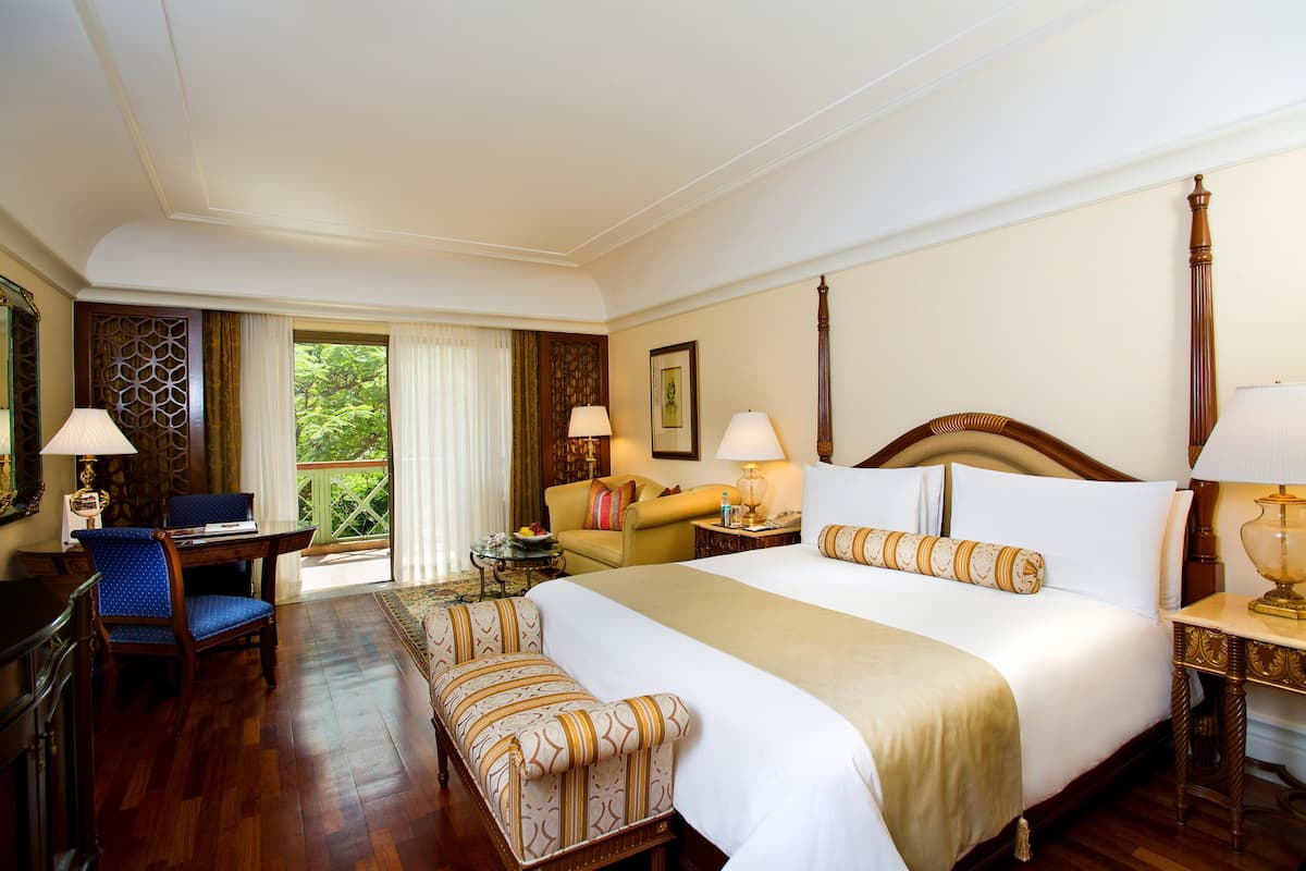 Habitación de hotel con una cama grande, un escritorio, una silla, un sofá y vistas al exterior con zonas verdes.