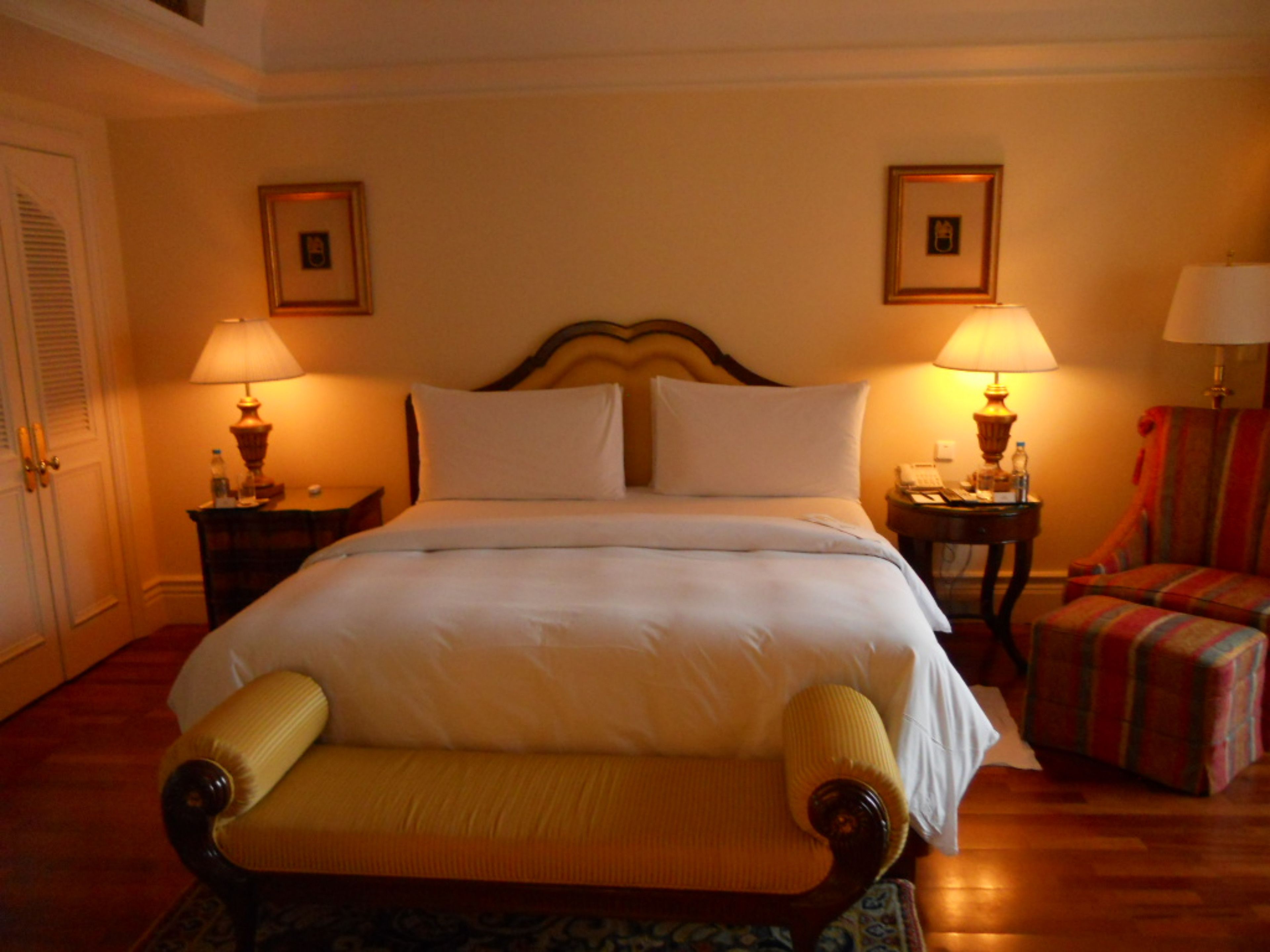 Ein Hotelzimmer mit einem großen Bett, zwei Nachttischen mit Lampen, einem Sessel und zwei gerahmten Bildern an der Wand.