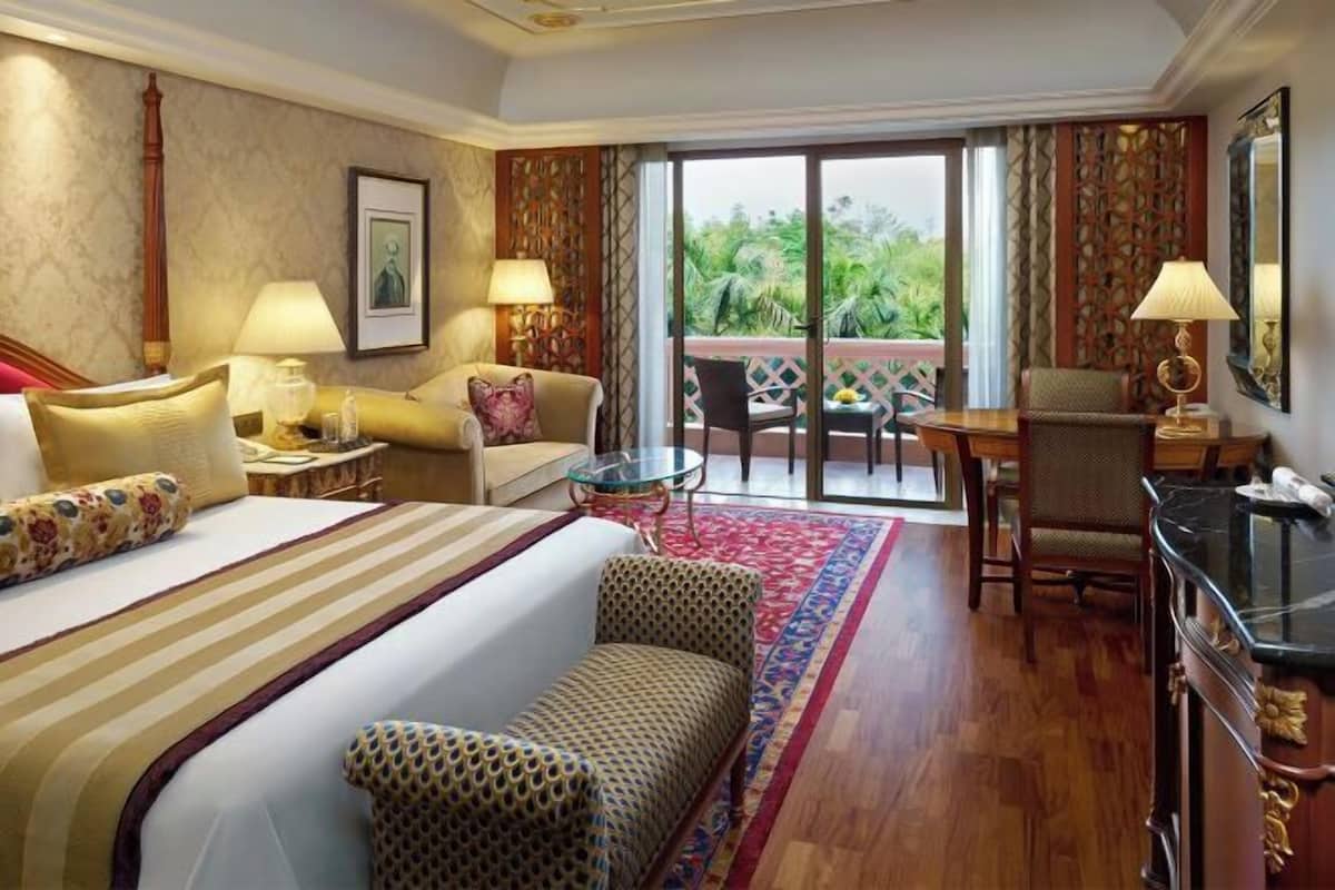 Habitación de hotel con cama, sofá, mesa de comedor y una silla. Se ve follaje a través de puertas de vidrio.