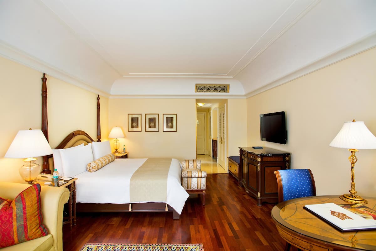 Una habitación de hotel con una cama, dos mesitas de noche, una silla, un escritorio, un televisor y una lámpara.
