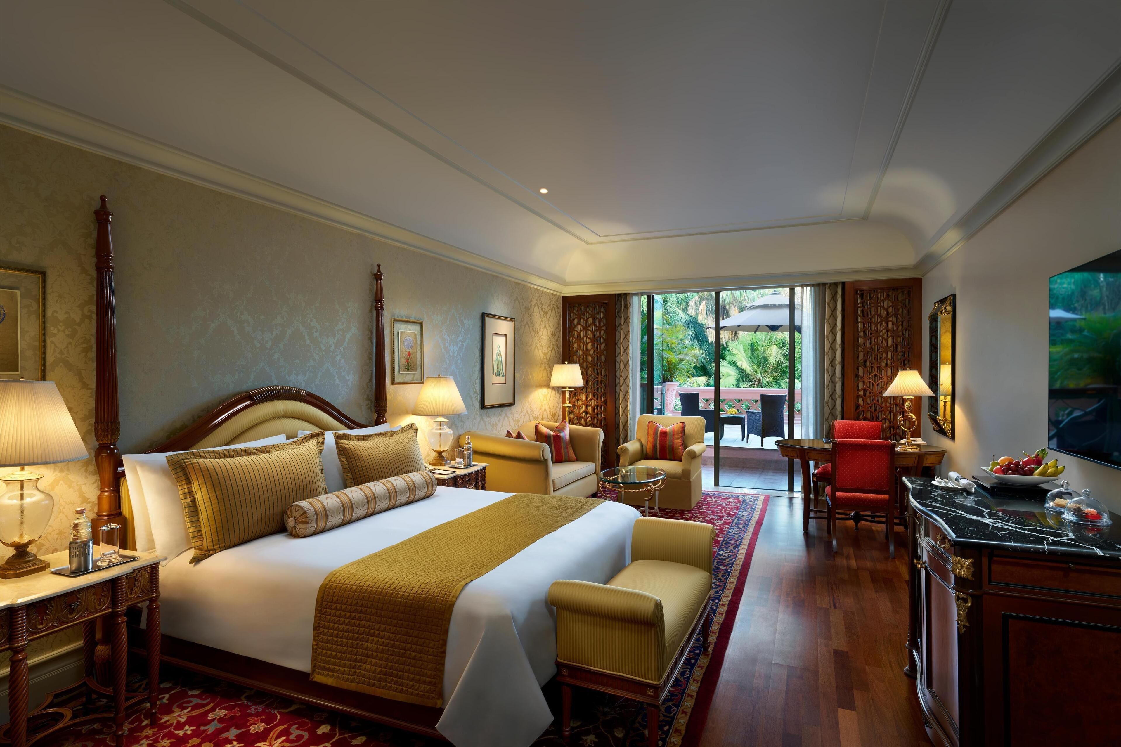 A hotel room with a large bed, two armchairs, a desk, and a dining area with a view of greenery.