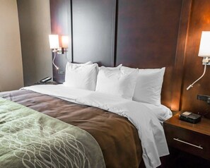 A hotel room with a neatly made bed, a bedside table with a phone and a digital clock, and two wall-mounted lamps.