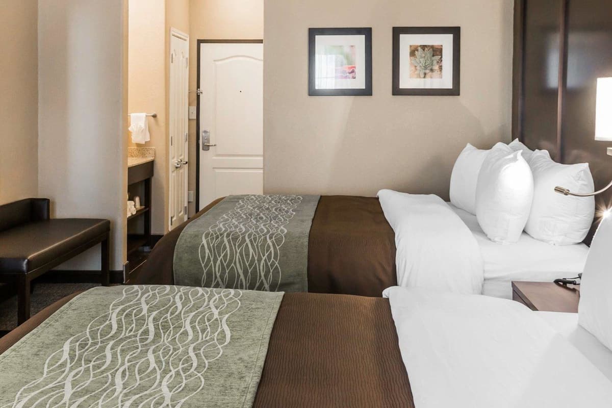 A hotel room with two beds, a desk, and a bathroom visible through an open door.