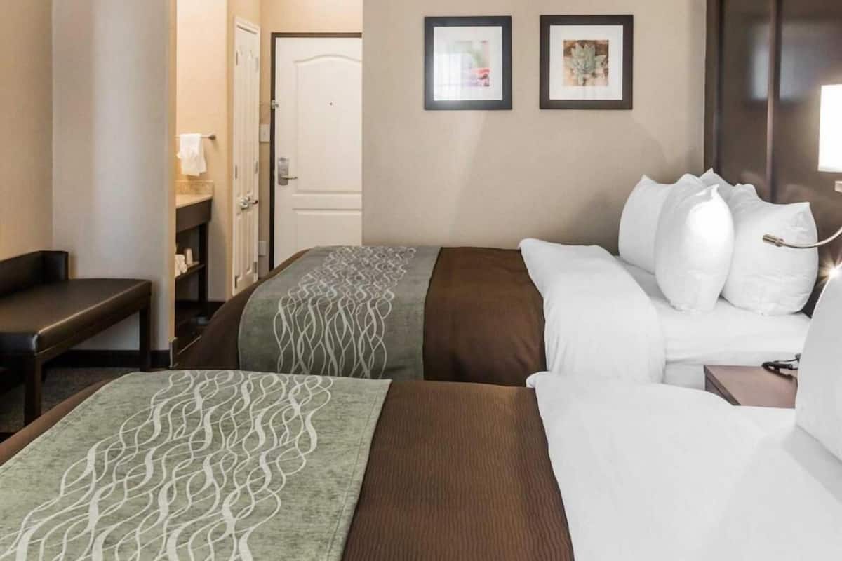 A hotel room with two beds, a desk, a chair, and a door leading to a bathroom.