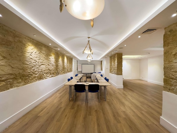 A conference room with a long table, blue chairs, a whiteboard, and a stone wall.