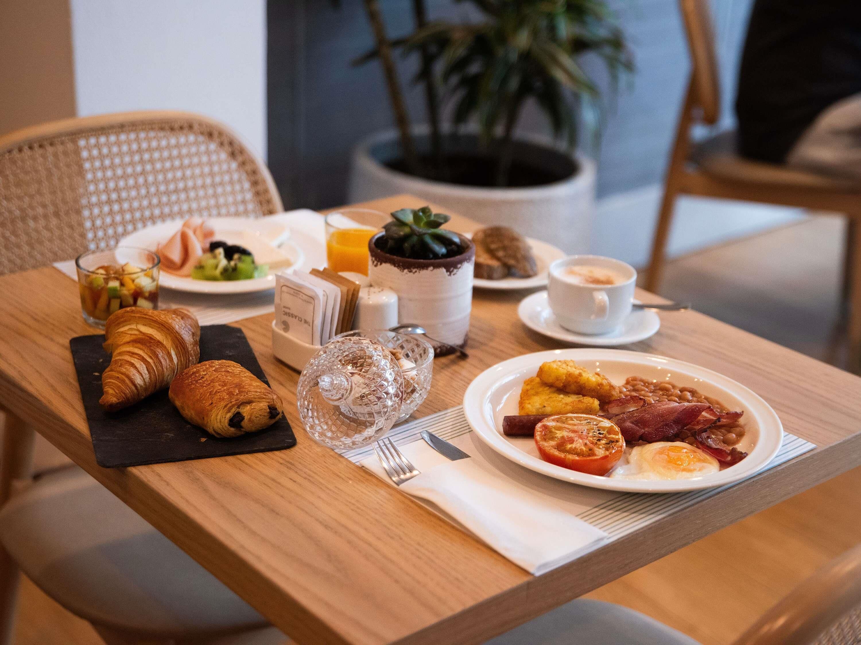 A breakfast setting with croissants, eggs, tomatoes, and coffee on a wooden table.