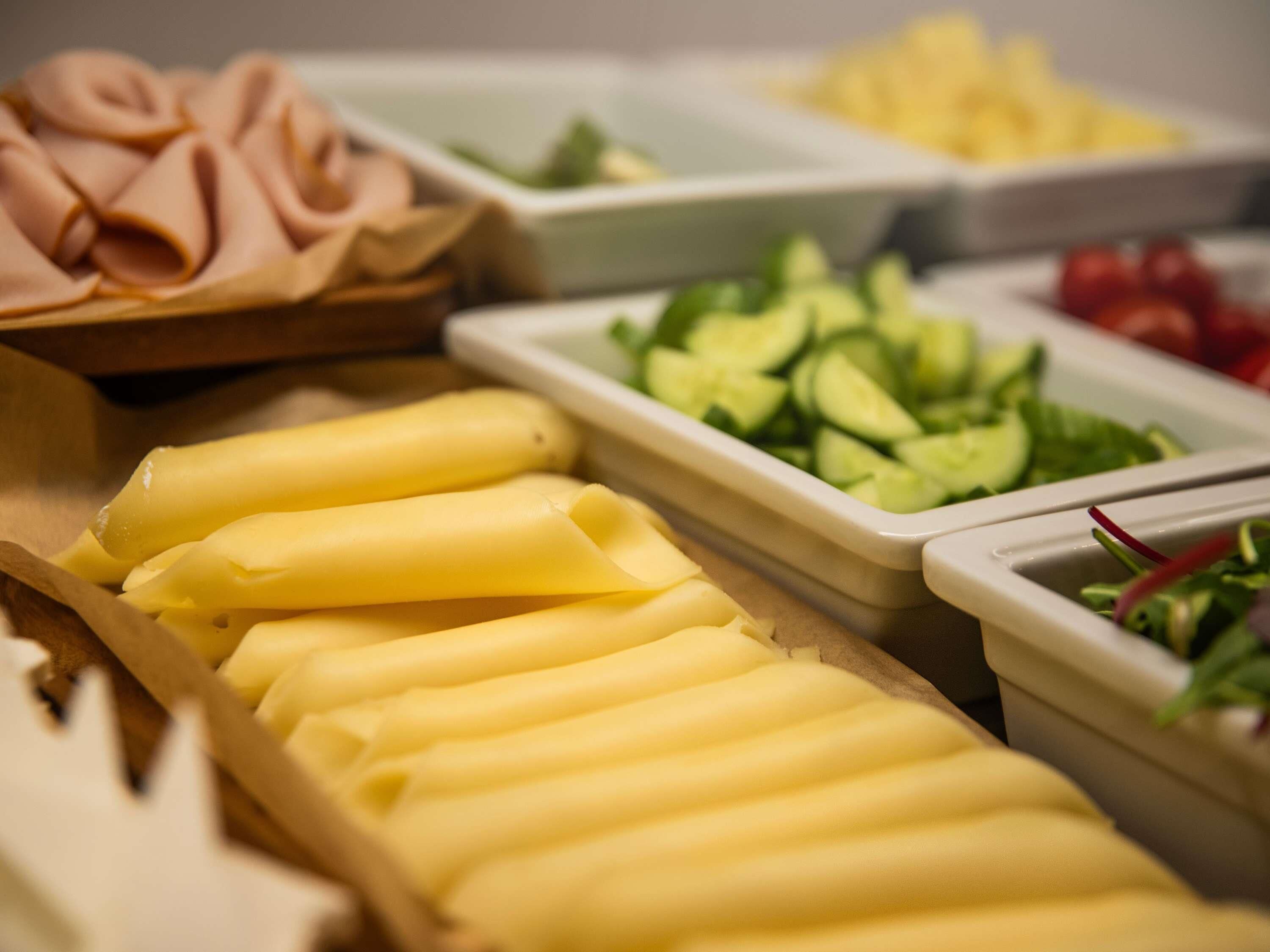 A buffet with various food items including sliced cucumbers, tomatoes, and a selection of cheeses.