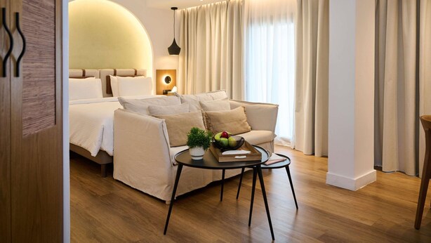 Une chambre d’hôtel moderne avec un lit, un canapé, une table ronde et des rideaux.