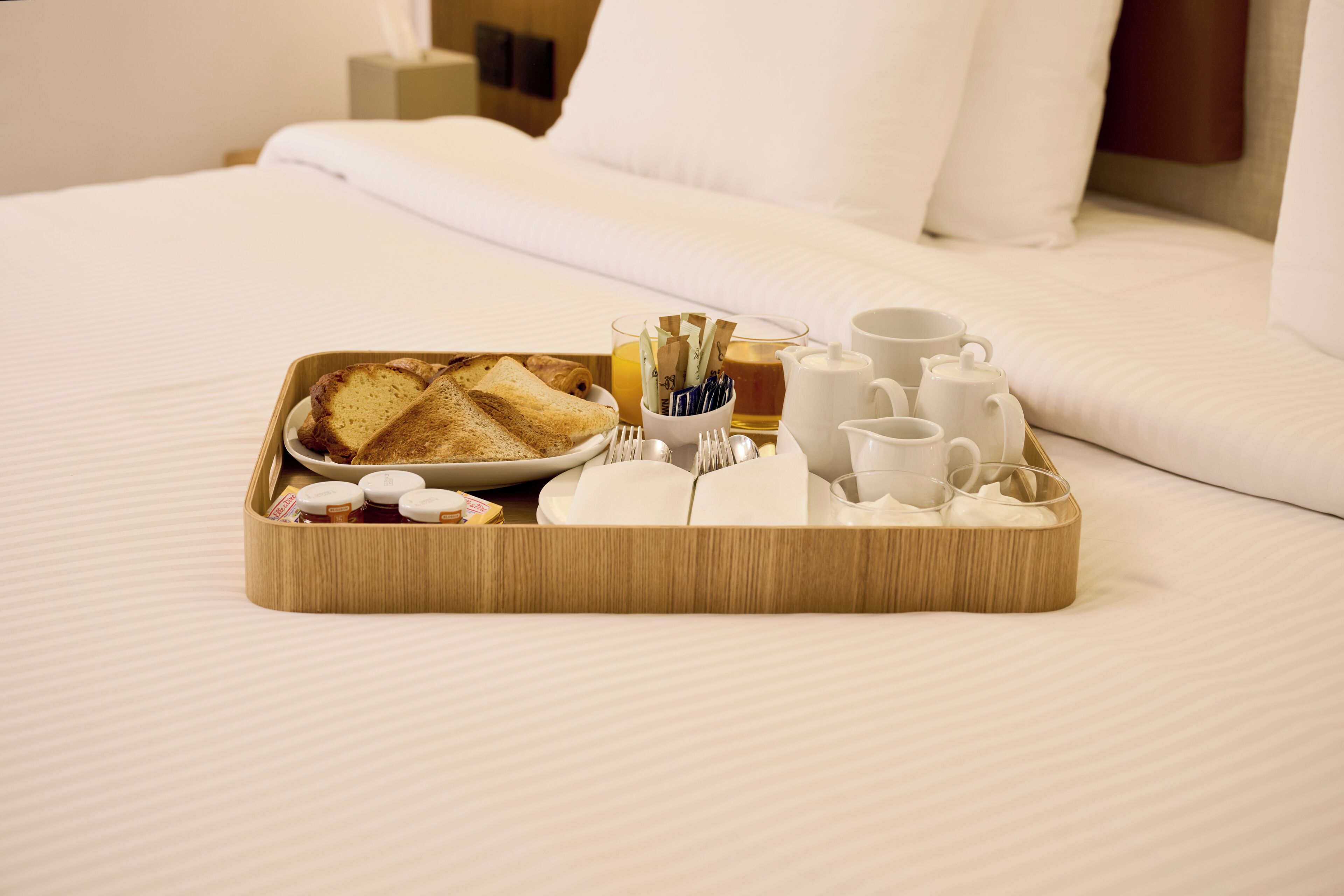 A neatly arranged breakfast tray on a bed with white linens, including toast, tea, and sugar packets.
