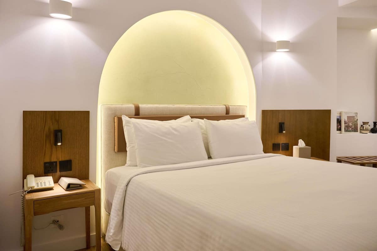 Hotellihuone, jossa on sänky, yöpöydät, puhelin ja lamppu.