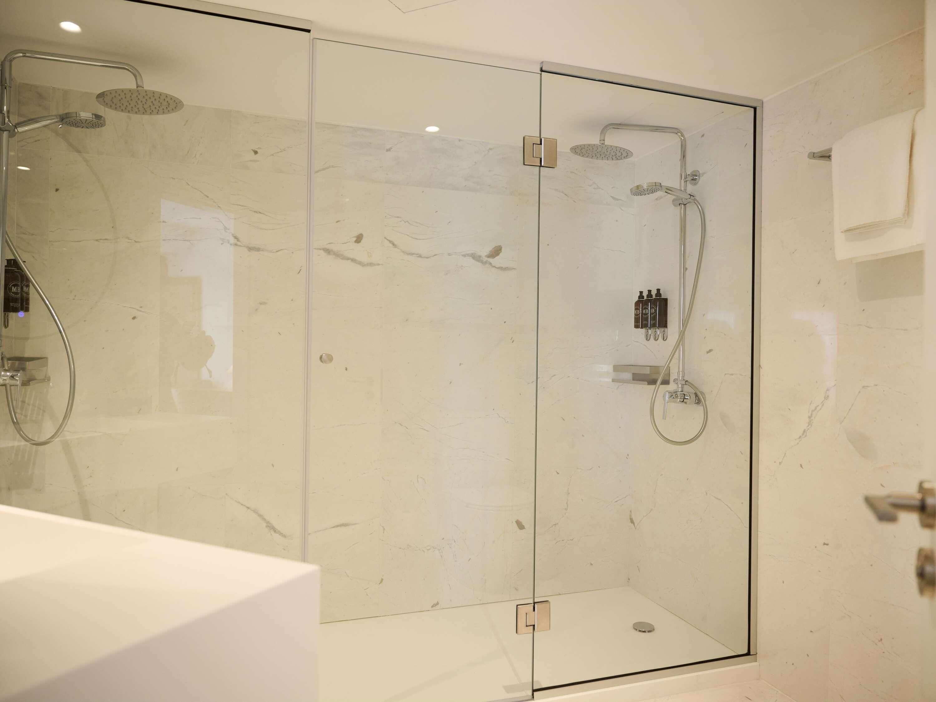 A modern glass-enclosed shower with a handheld showerhead and a wall-mounted faucet.