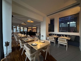 Un restaurante moderno con mesas largas, sillas blancas y una zona de bar.