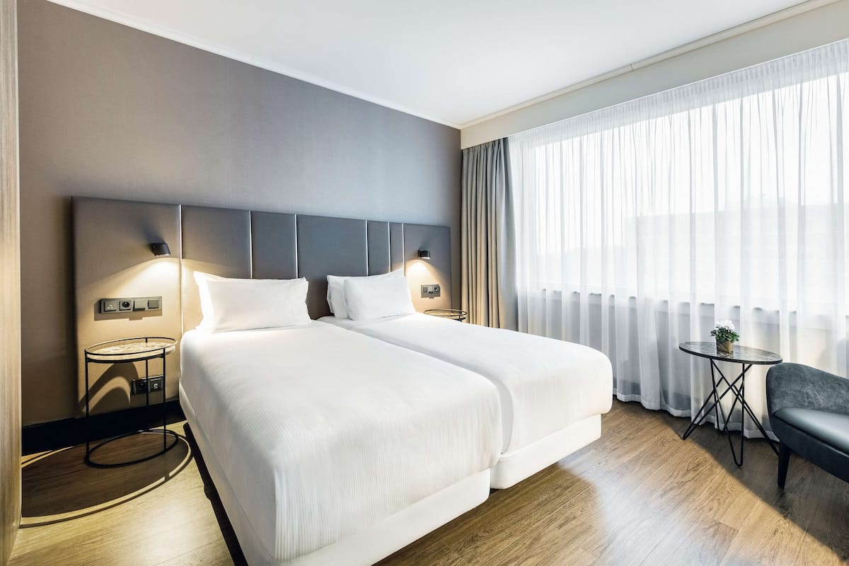 A hotel room with two beds, a small table, and a chair.