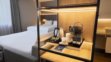A hotel room with a bed, a bedside table with a kettle, cups, and a tray of snacks.