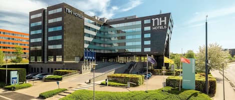 Un hotel moderno con un llamativo letrero de 'NH Hotels', un área de entrada bien cuidada y un jardín ajardinado.