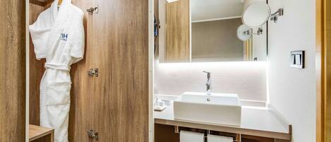 A modern bathroom with a wooden vanity, a large mirror, and a robe hanging on a hook.