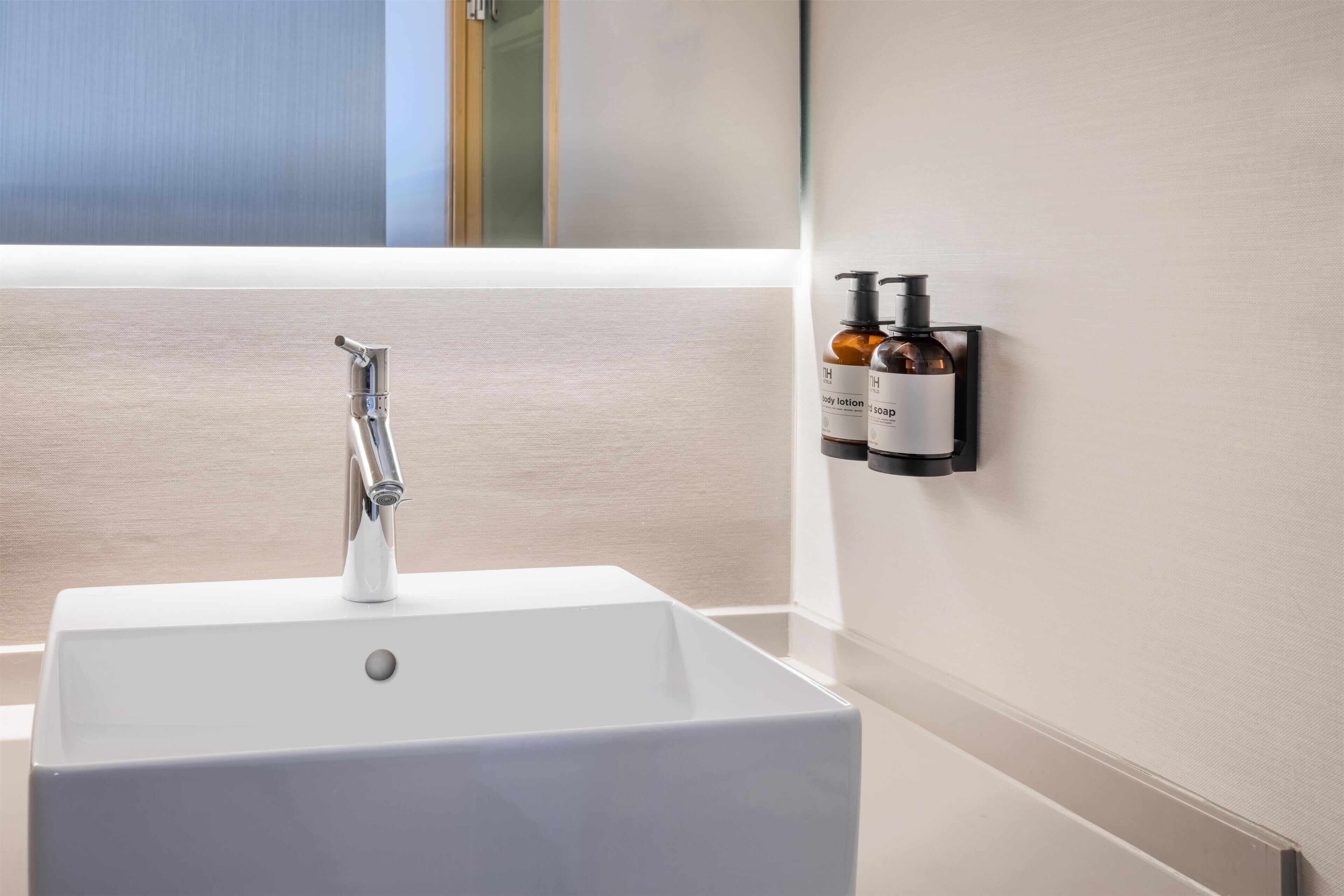 Une salle de bain moderne avec un lavabo blanc, un robinet chromé et deux distributeurs de savon fixés au mur.