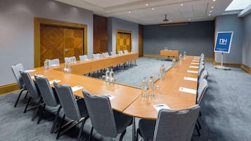 A conference room with a long table, chairs, water bottles, and a sign for NH Hotels.