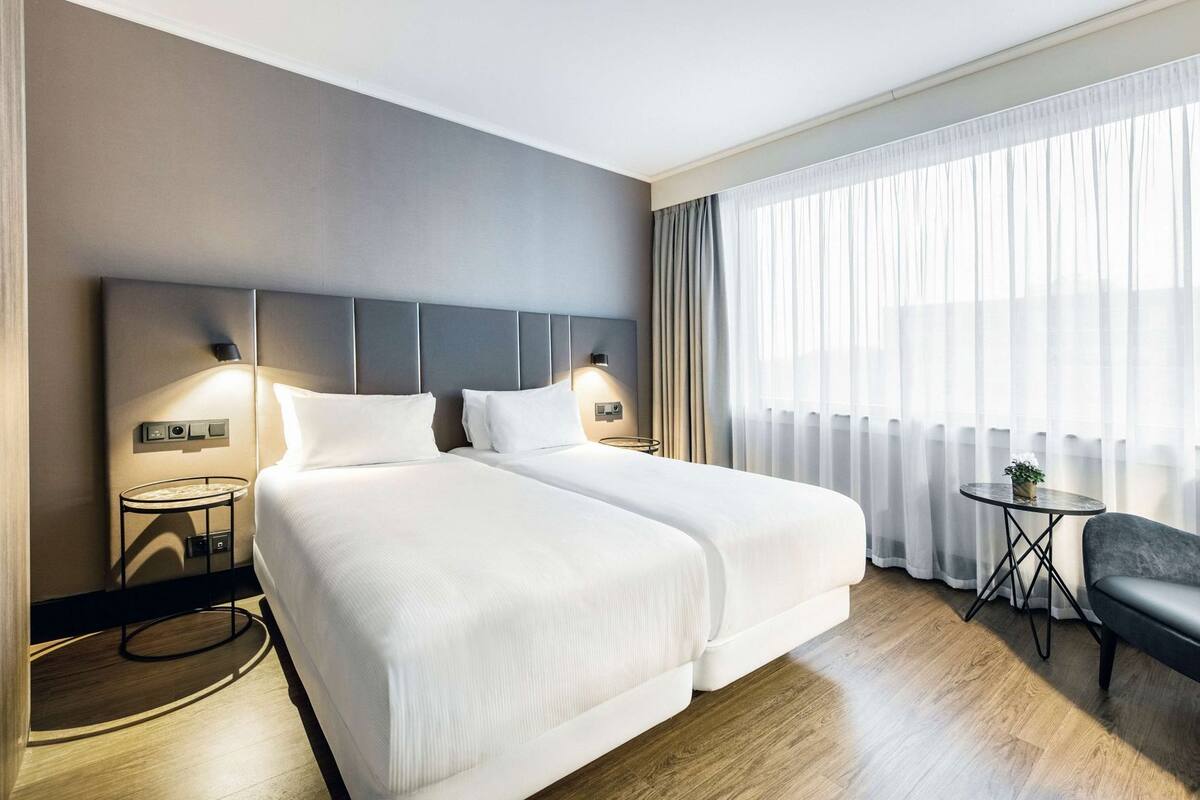 A hotel room with a large bed, bedside tables, a small round table, and a chair.