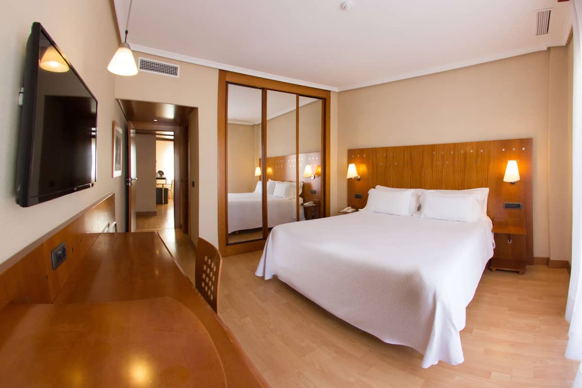 A hotel room with a large bed, bedside lamps, a flat-screen TV, and a wooden headboard.