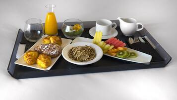 A breakfast tray with croissants, cereal, fruit, and a glass of orange juice.