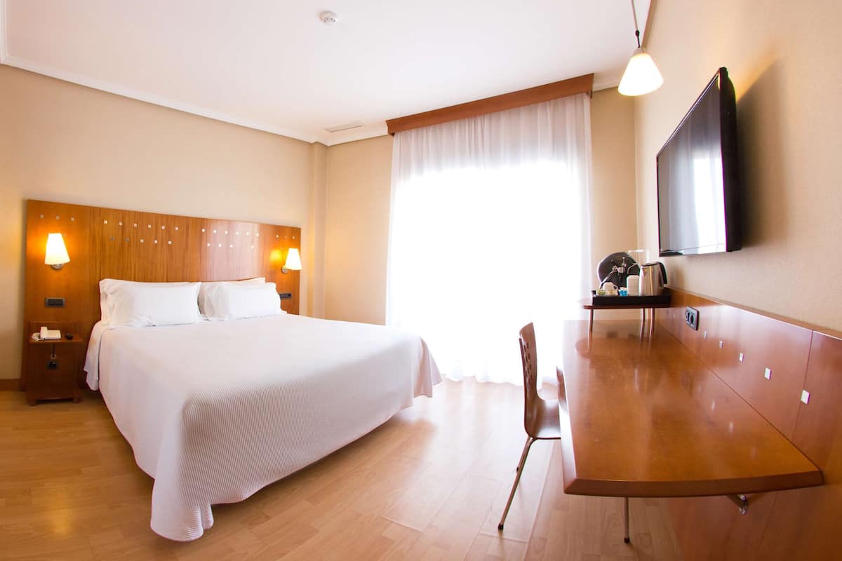 A hotel room with a large bed, bedside lamps, a flat-screen TV, a wooden desk, and a chair.