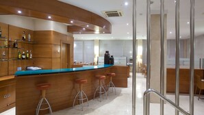 A modern bar area with wooden cabinets, a blue countertop, and three stools. - NH San Pedro (Marbella)