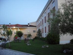 Un edificio con techo de tejas rojas, patio empedrado y un pequeño jardín con rocas y arbustos.
