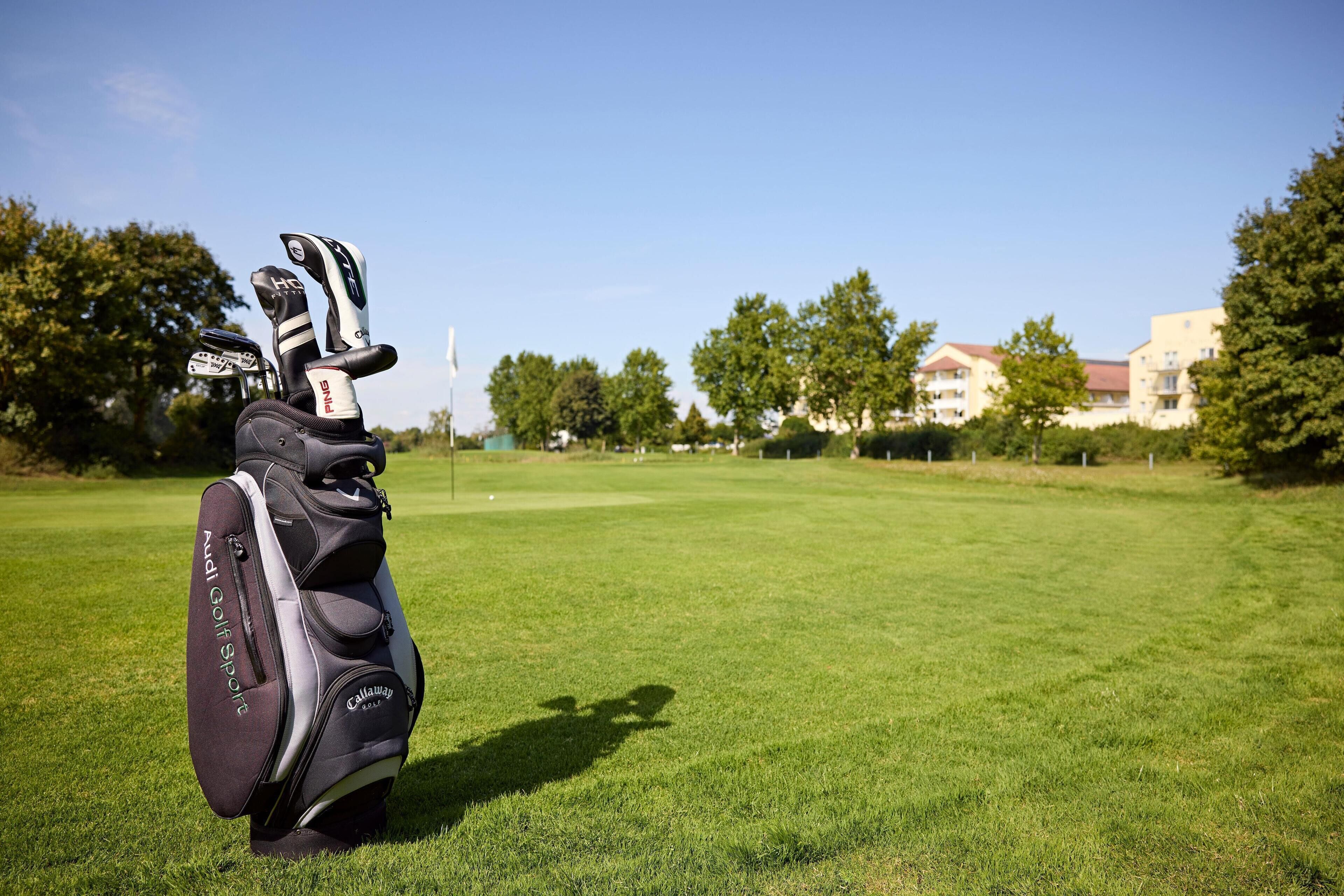 A golf bag on a well-maintained grass field with trees and buildings in the background.
