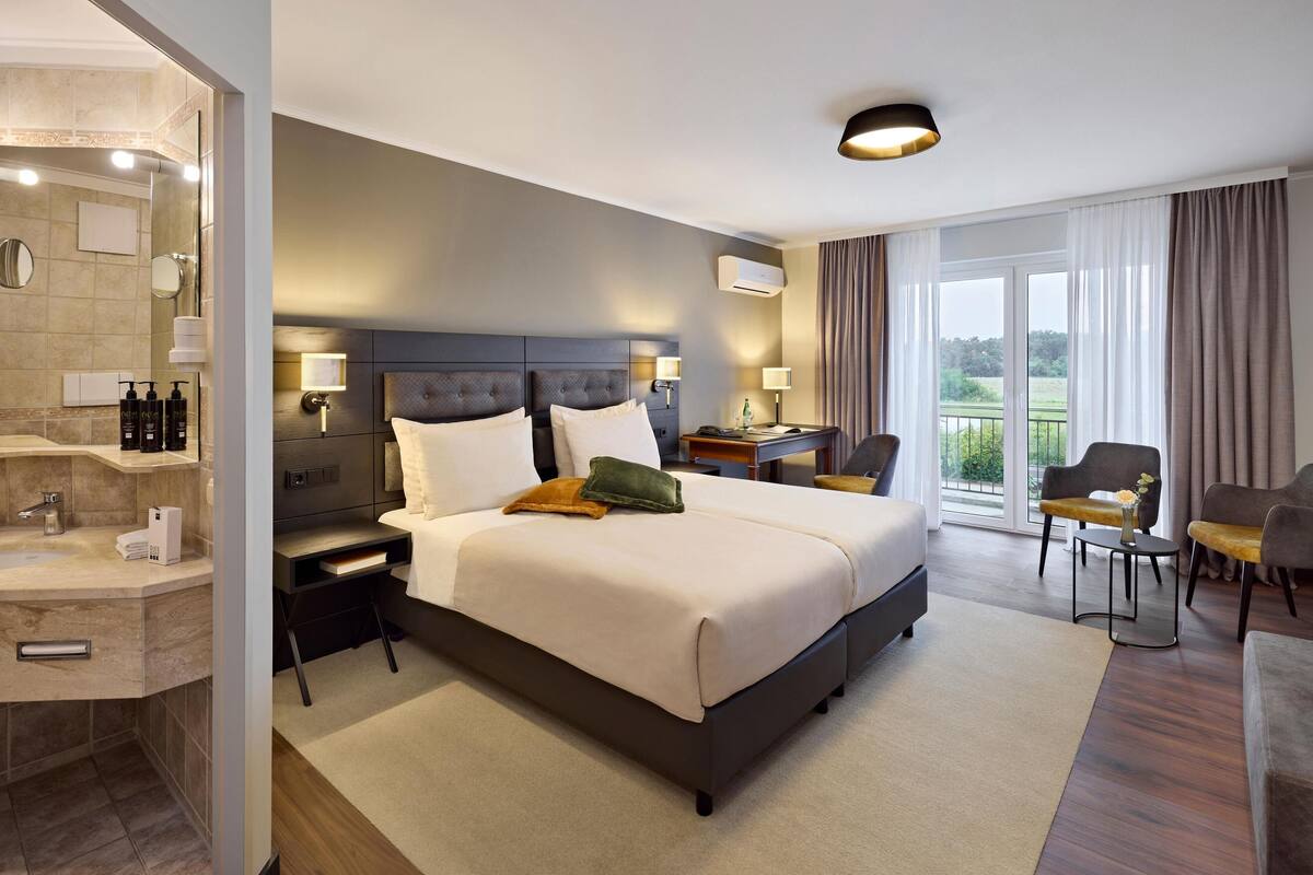 A modern hotel room with a large bed, bedside tables, a desk, and a view of the outdoors.