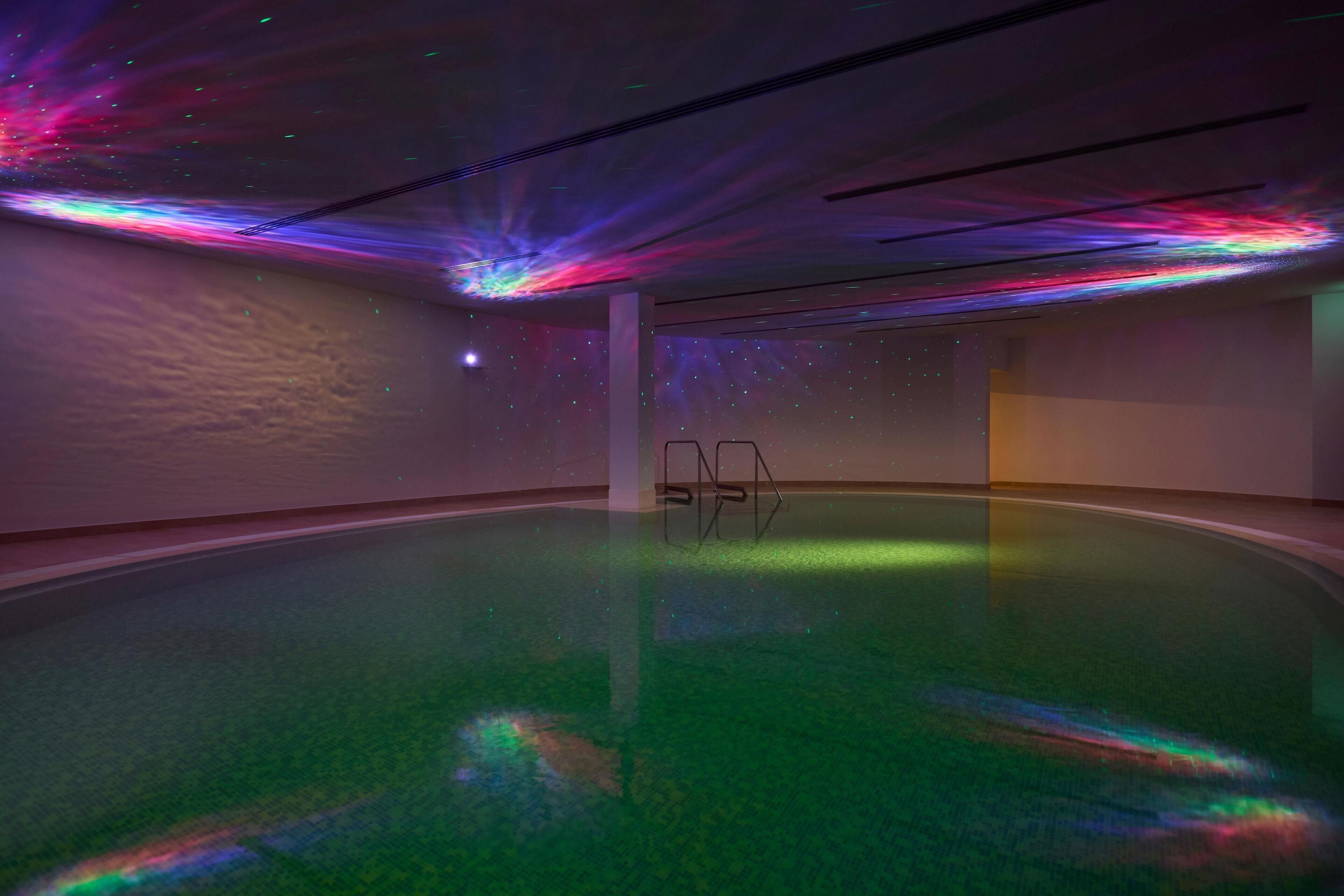 Una piscina interior con una proyección de luces coloridas en el techo y un diseño moderno y sencillo.