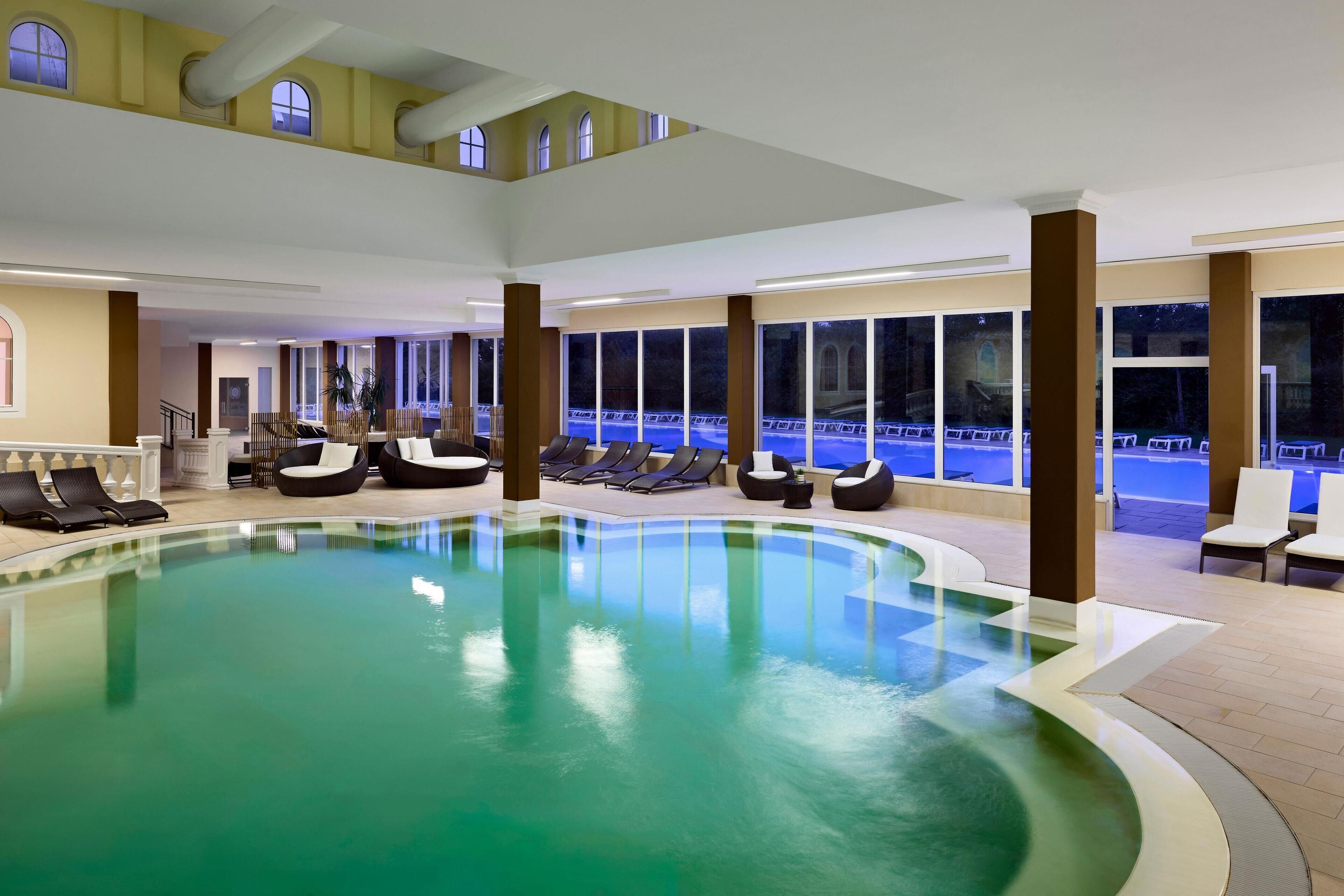 An indoor swimming pool with lounge chairs and a view of the outside.