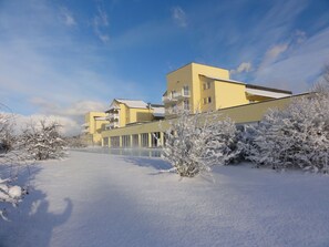 Ein gelbes Gebäude mit mehreren Balkonen, umgeben von schneebedeckten Bäumen und wolkenlosem Himmel.