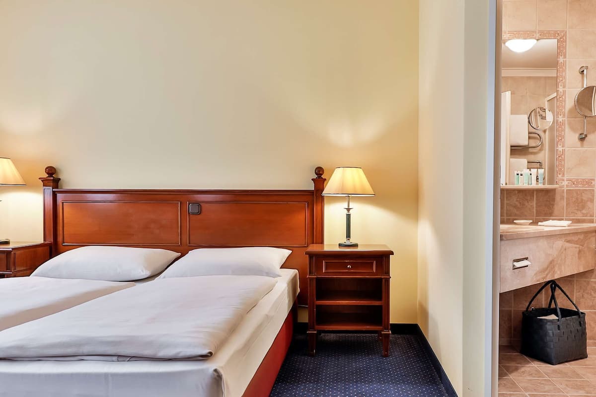 A hotel room with two beds, a nightstand with a lamp, a bathroom with a mirror, and a black bag on the floor.