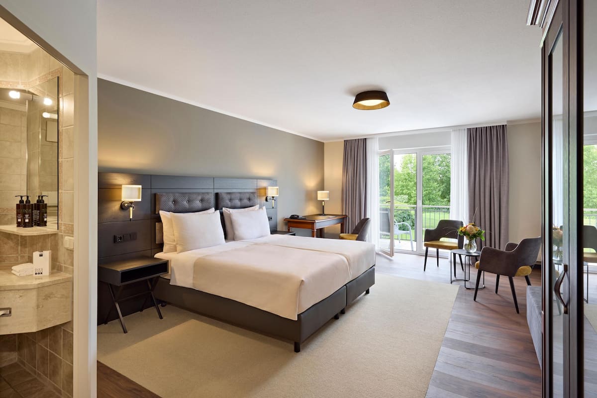 A modern hotel room with a large bed, bedside tables, a desk, and a seating area with chairs.